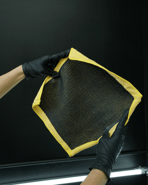 A detailer wearing black gloves holding a yellow clay cloth on a black background 