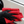 Person cleaning a white car with a red microfibre and black gloves