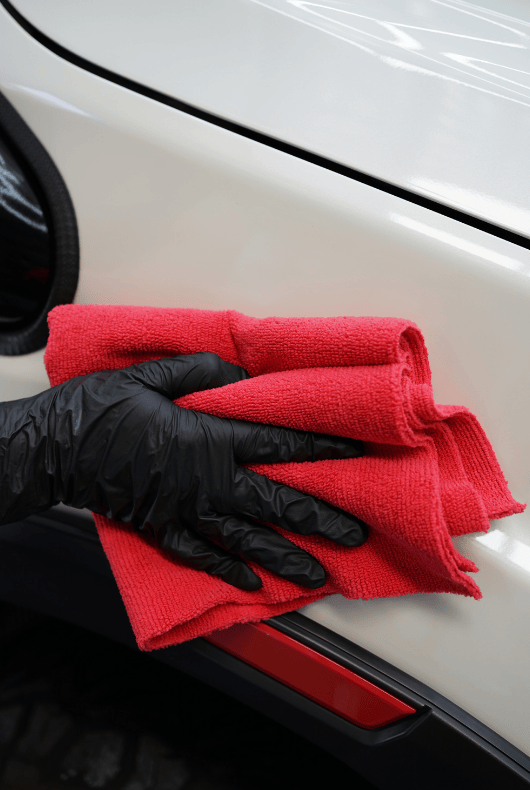 Person cleaning a white car with a red microfibre and black gloves