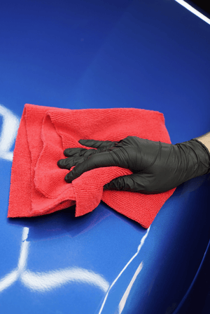 Person cleaning a blue car with a red microfibre and black glove