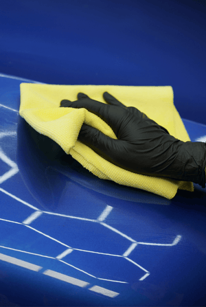 Hand wearing a black glove cleaning a blue surface with a yellow cloth