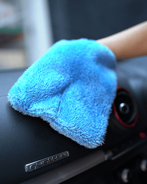 A person holding a blue car interior scrub mitt cleaning a dashboard