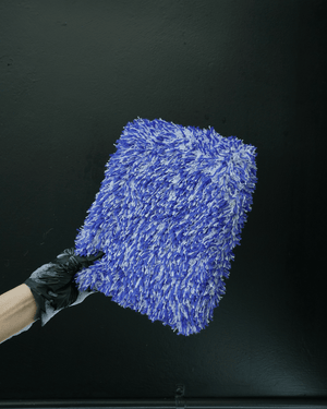 A detailer wearing black gloves holding a large car wash pad on a black background