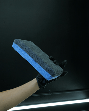 A person wearing black gloves holding a grey and blue extra large microfibre coating applicator pad