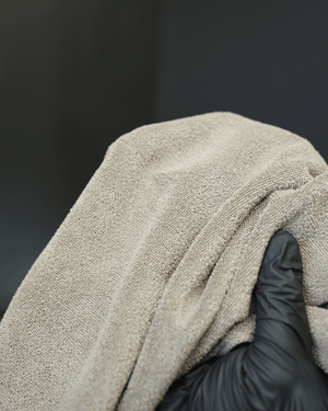 A person holding a brown microfibre cloth close up to the camera with black gloves on