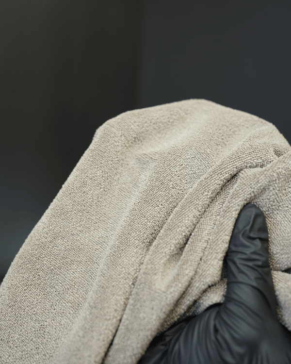 A person holding a brown microfibre cloth close up to the camera with black gloves on
