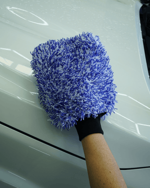 A detailer washing a white car with a blue and white microfibre wash mitt