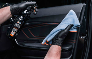 A person wearing black gloves holding a blue towel with a orange border in front of a car door
