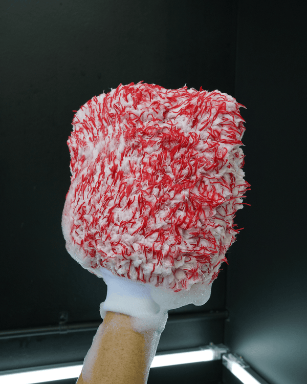 A detailer holding a red and white car wash mitt on a black background