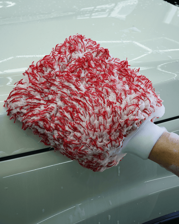 A detailer using a red and white car wash mitt to wash a white car 