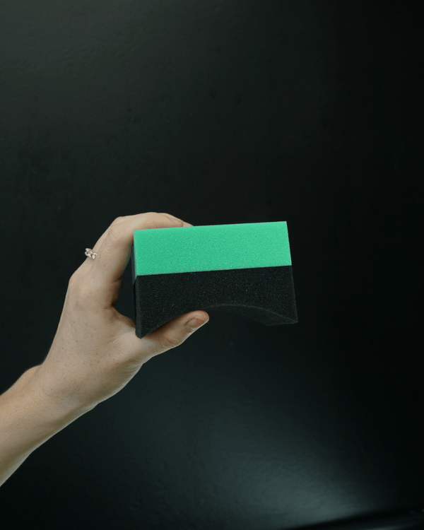 A person holding a green and blue tyre dressing applicator on a black background