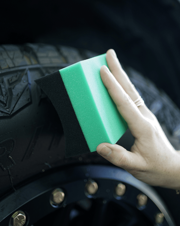 A person using a black and green tyre dressing applicator on a tyre