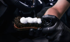 Detailer applying foam cleaning product onto a natural bristle brush for interior cleaning