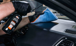 Hand in black glove cleaning a leather or plastic dashboard with ADBL Interior Cleaner and blue microfibre