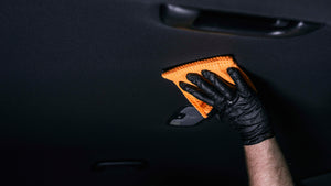 Hand in black glove gently cleaning a dark car headliner with an orange microfibre towel and ADBL BONNET