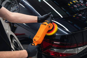 Detailer using ADBL Roller D15 Polisher (orange) with foam polishing pad on a black car trunk/body panel