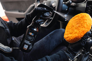 Person in black glove applying ADBL Leather Conditioner with a blue microfibre pad to a black car leather seat