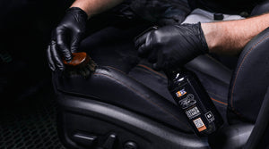 Person applying ADBL INTERIOR QD with a spray bottle and leather brush towel to a car seat