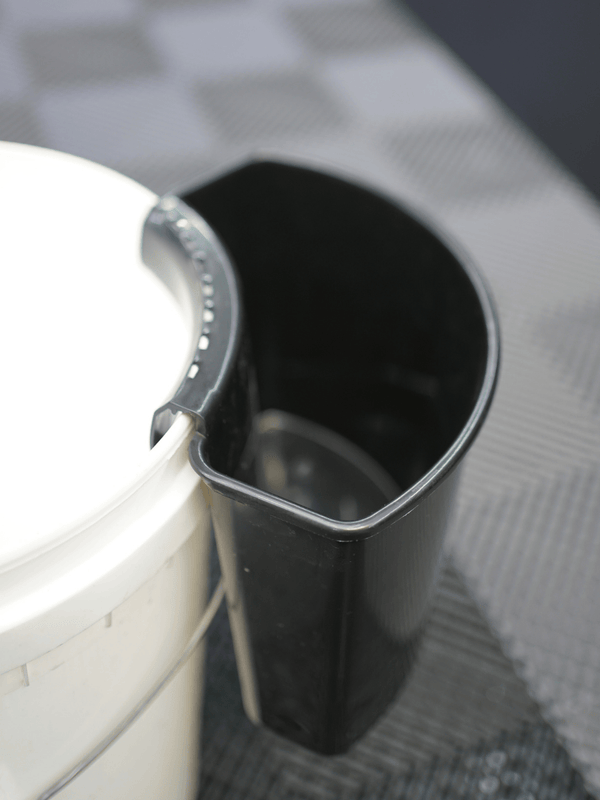 A black car wash bucket tool holder on a white bucket