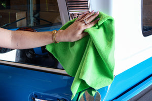A person cleaning a white and blue car with a green cloth
