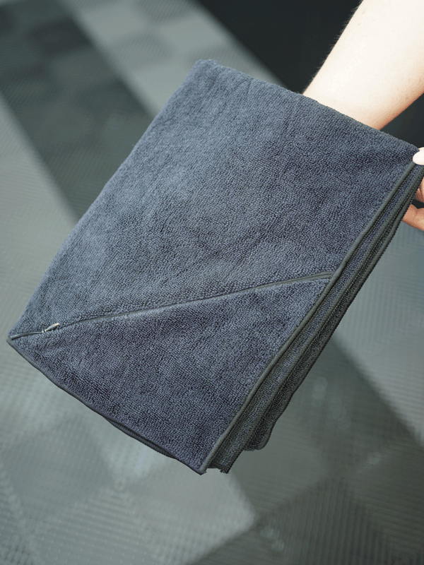 Grey microfibre towel held by a hand on a reflective surface