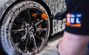 Person detailing a dirty car wheel with foam using an ADBL Wheel Dagger brush