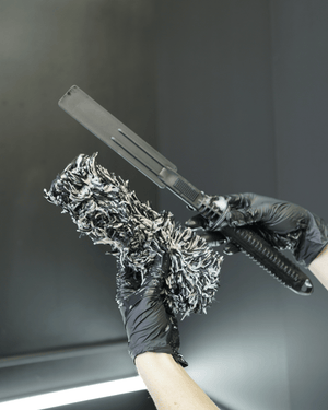 A person with black gloves on holding p a black and white microfibre wheel woolie tyre cleaning tooll